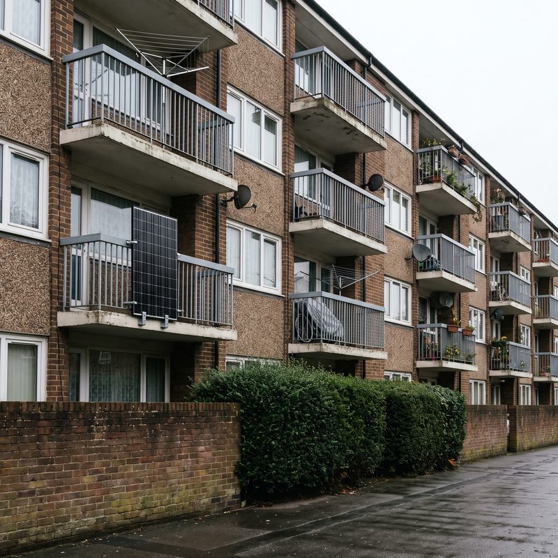 Illustration: a British block of flats with one solar panel hung on a balcony railing